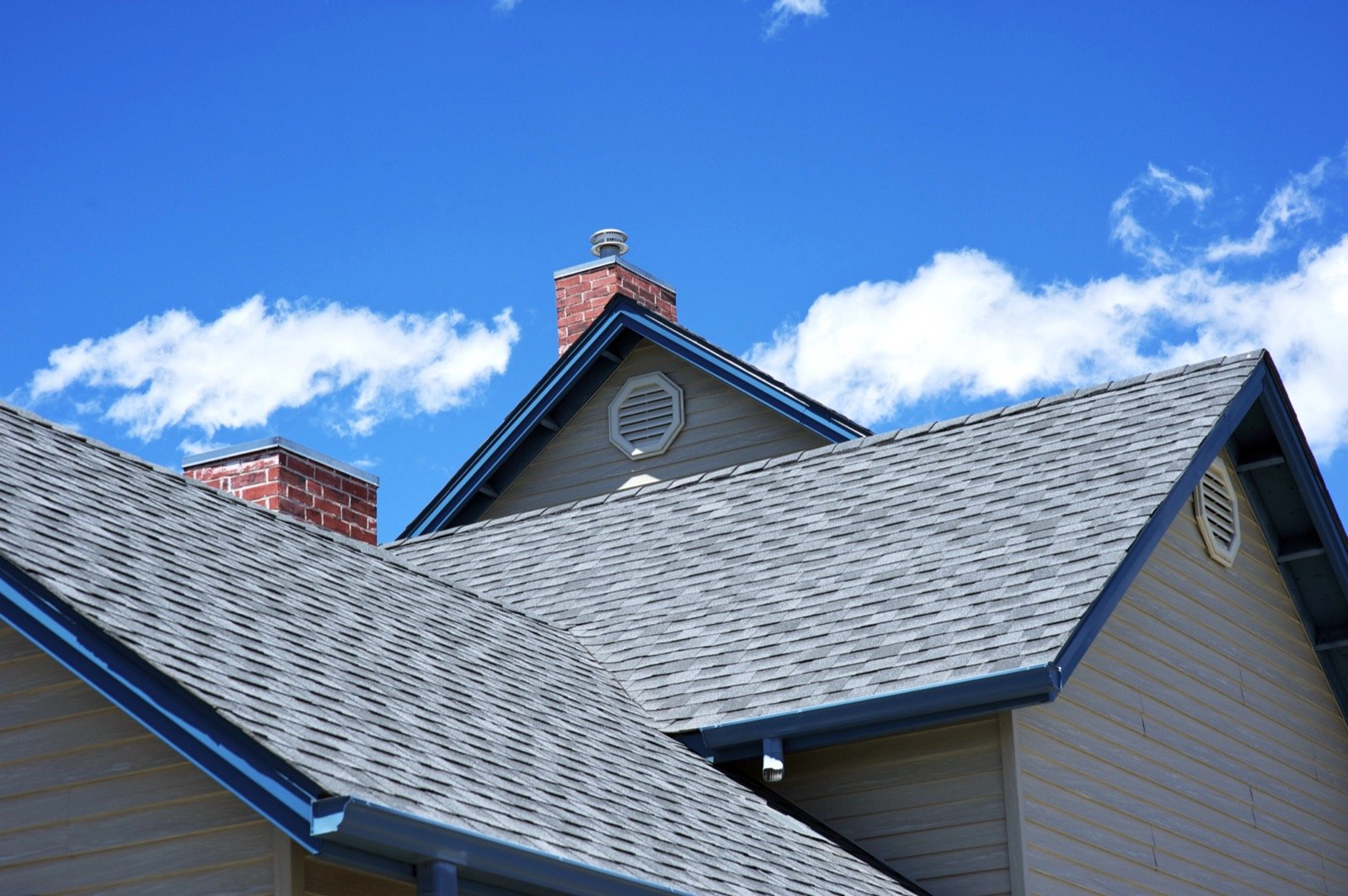 Residential roof with asphalt shingles, brick chimneys, and siding by Gerhard and Sons